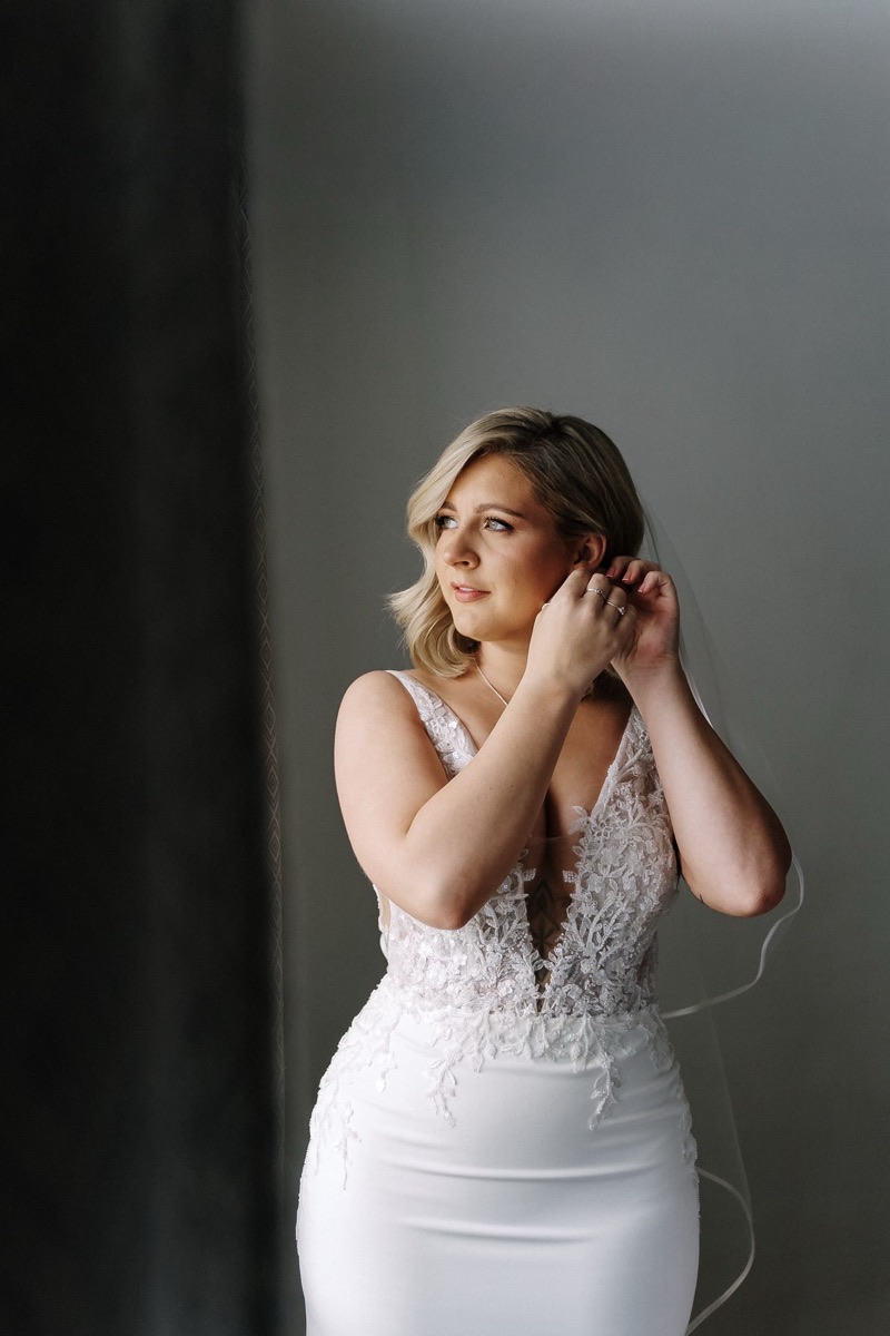 Bride in window light putting on earrings