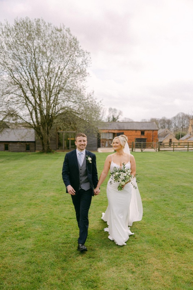 Bride and groom walking hand in hand across the lawn